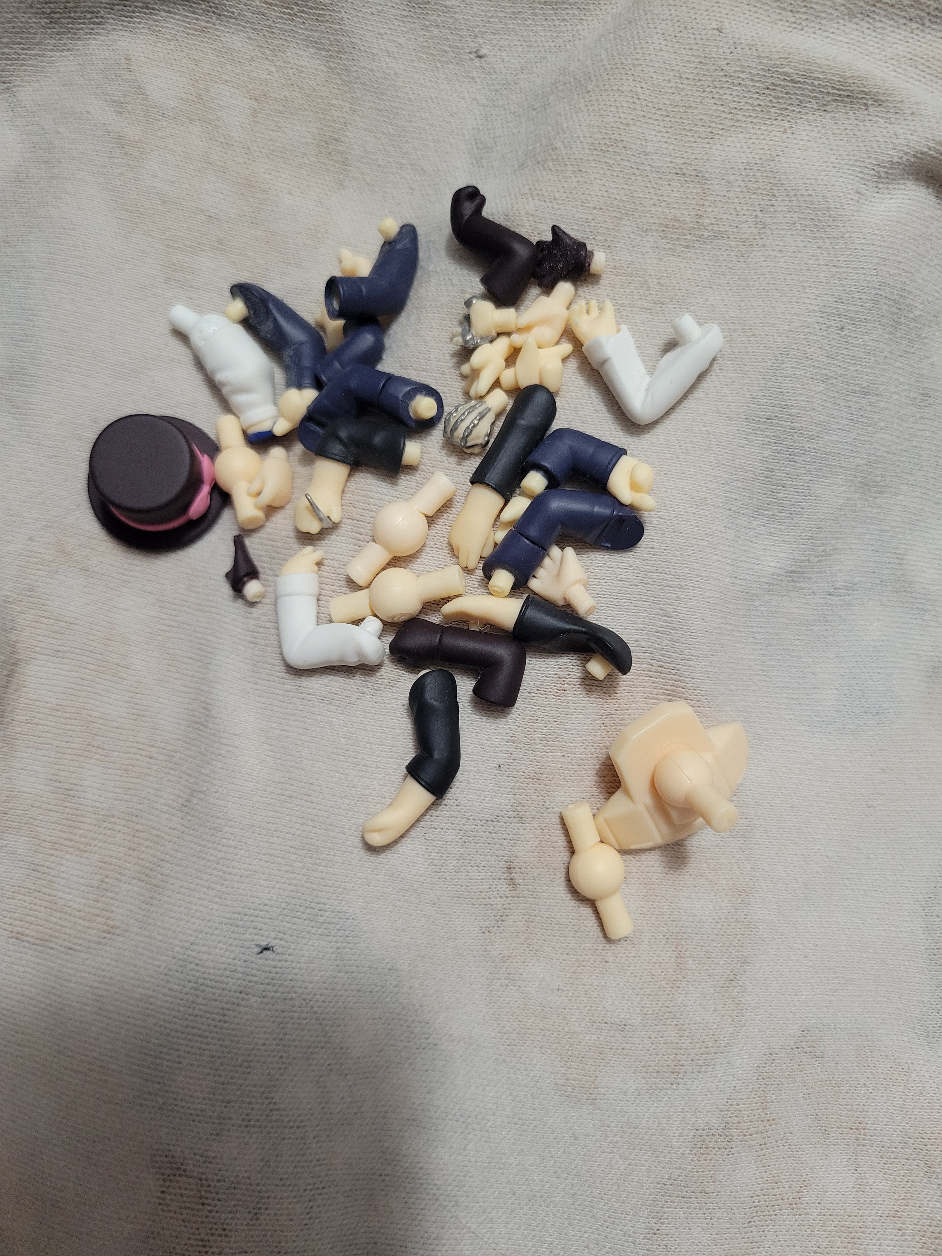 Small pile of nendoroid hands and hat on a white cloth.